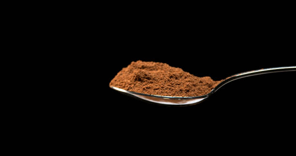 Nutmeg, myristica fragans, Powder falling from Spoon against Black Background