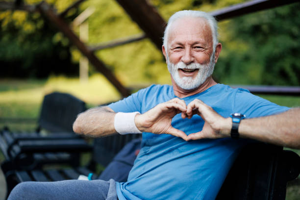 Portrait of a senior sporty man in nature showing a heart-shaped symbol