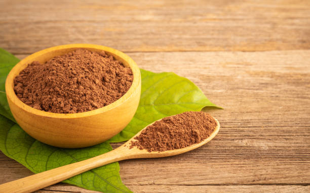 Close up Cocoa powder in wooden bowl and green leaf on wooden table background