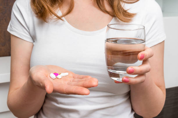 Pile of pills and glass of water in female hands - health care concept