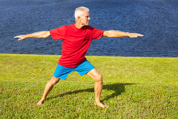 Full length of fit senior man doing yoga warrior pose on lakeshore